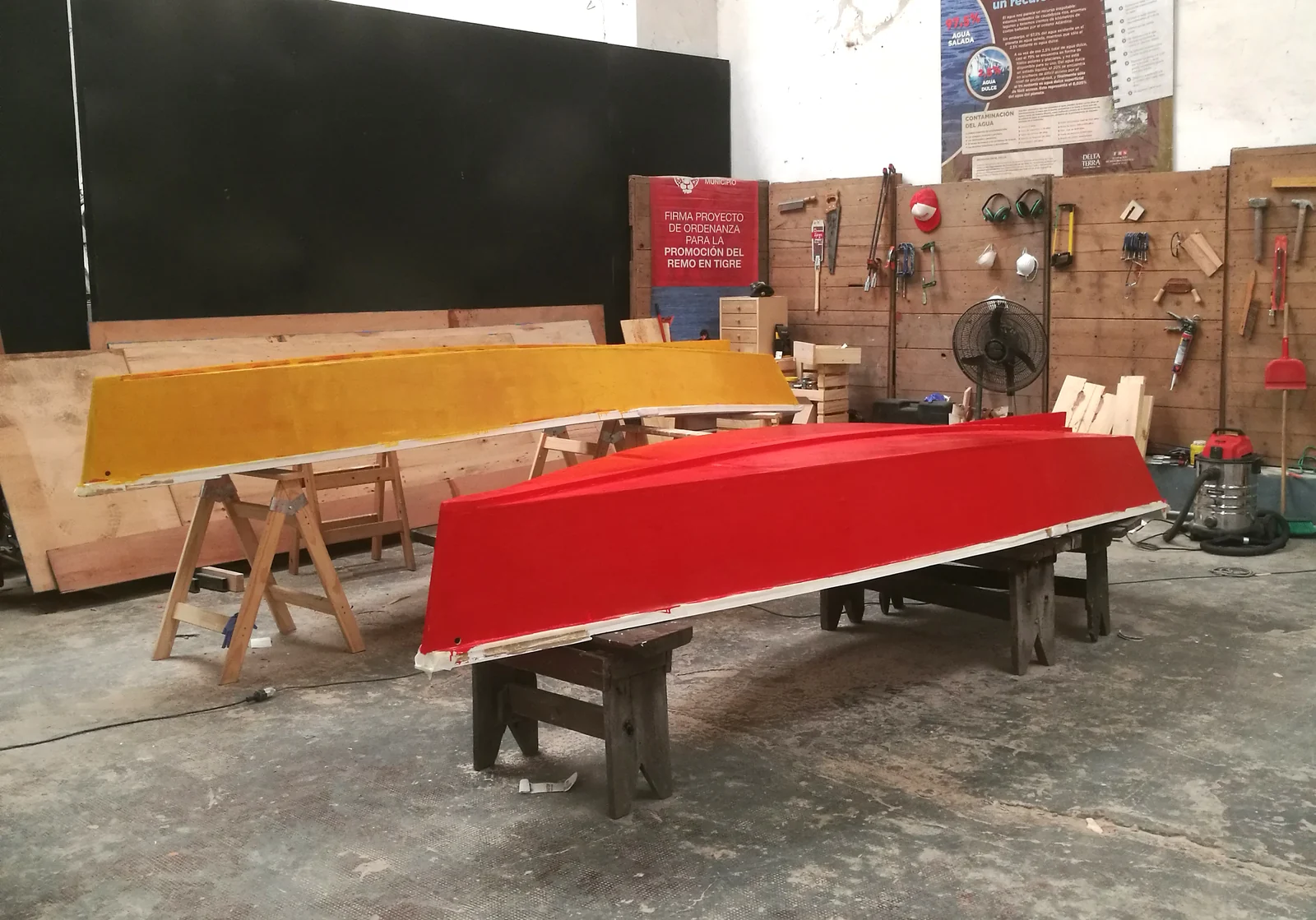 Un casco de bote pintado de rojo, boca abajo sobre caballetes, en el galpón.