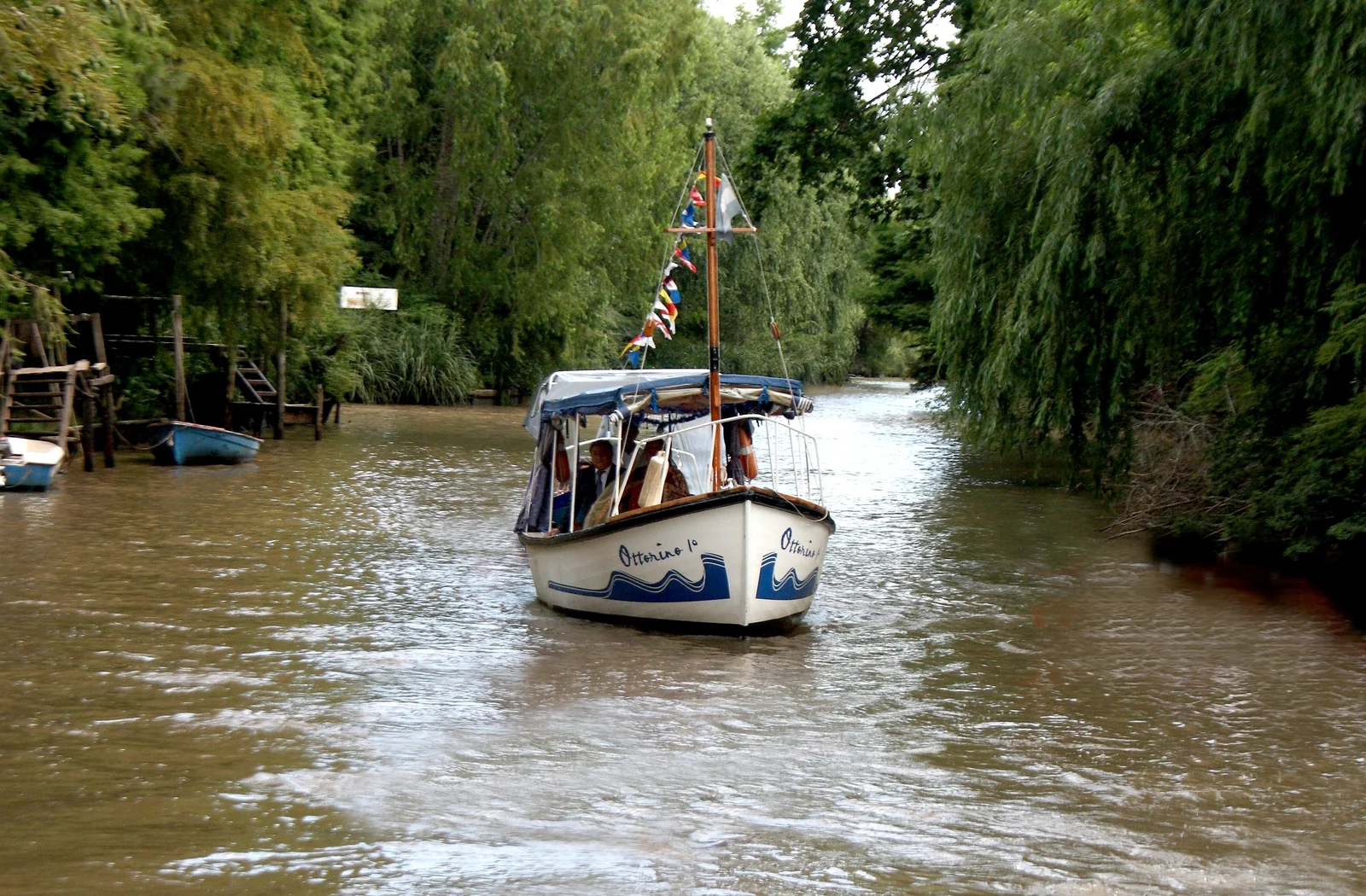 Un río del Delta de Tigre rodeado de árboles, con una lancha de pasajeros navegando.