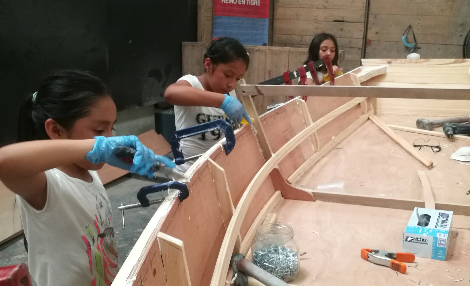 Una chica con guantes aplica adhesivo en el interior del casco de un bote en construcción.