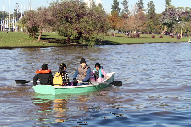 Chicos con chaleco salvavidas reman con un adulto en un bote verde