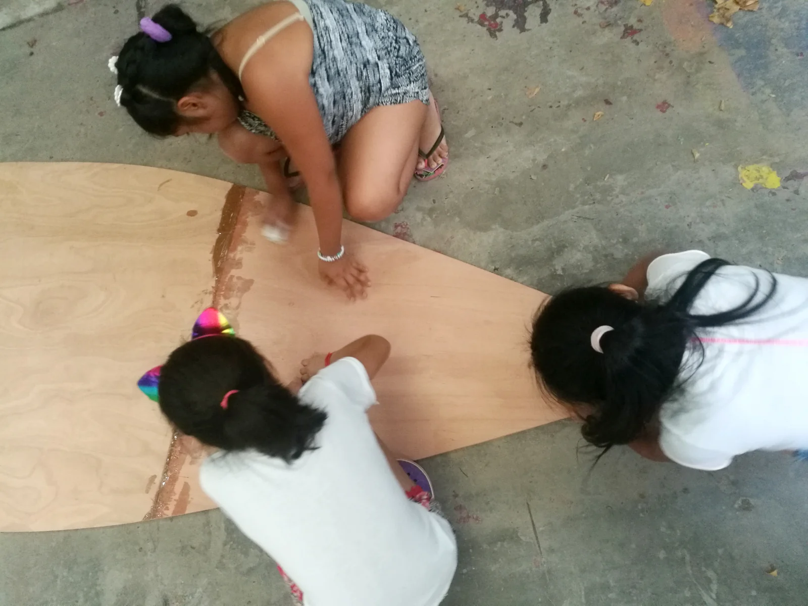 Dos chicas, vistas desde arriba, trazan líneas sobre una plancha de madera en el piso del taller.